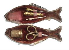 two fish shaped objects sitting on top of each other in a wooden case with gold trimmings