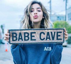 a woman holding up a wooden sign that says babe cave in front of her face