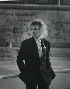 black and white photograph of a woman leaning against a fence with her hands in her pockets