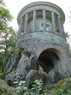 an old stone structure with a round window in the center surrounded by trees and rocks