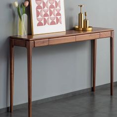 a wooden table with flowers on it next to a framed art print and two vases