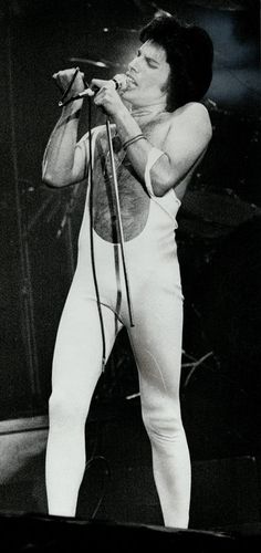 a man in white is singing on stage with his hands up to his mouth and holding a microphone