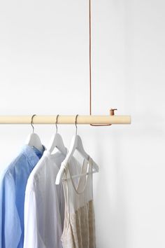 three shirts hanging on a clothes rack in front of a white wall with a wooden hanger