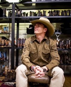 a man wearing a cowboy hat sitting on a chair in front of a rack of shoes