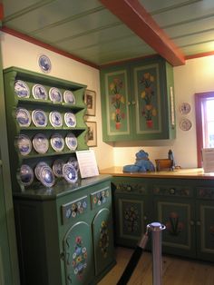 an old fashioned kitchen with green cabinets and plates