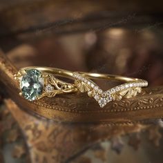 two gold rings with green and white stones on them sitting on a leafy surface