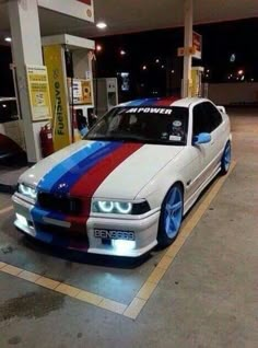 a white car with red, blue and green stripes parked in a gas station at night