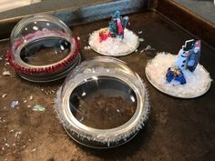 three snow globes sitting on top of a counter next to a bowl filled with sand