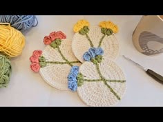 three crocheted coasters with flowers on them next to yarn and knitting needles