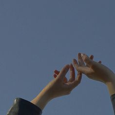 two hands reaching up into the air to catch a frisbee in the sky