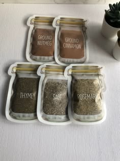 four jars filled with different types of spices on top of a white tablecloth next to a potted plant