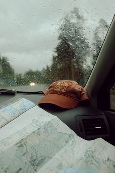 a hat is sitting on the dashboard of a car with raindrops and trees in the background