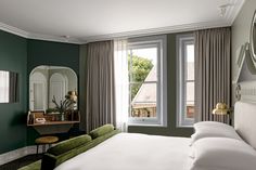 a bedroom with green walls and white bedding, two mirrors on the wall above it