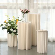 three white vases with flowers in them sitting on the floor next to each other