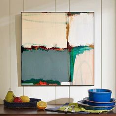 an abstract painting hangs on the wall above a table with blue dishes and fruit in bowls