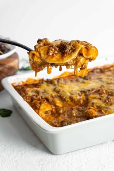 a spoon full of lasagna casserole being lifted from a white dish