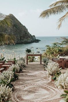 an outdoor ceremony setup with flowers and greenery on the ground next to the ocean