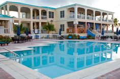 an empty swimming pool surrounded by chairs and umbrellas in front of a large building