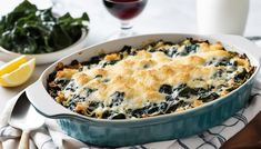 a casserole dish with spinach and cheese on top, next to a glass of red wine