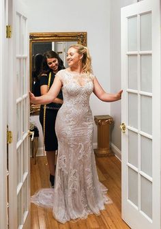 a woman in a wedding dress is looking at herself in the mirror while another woman looks on