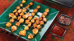 several skewers of chicken on a green plate with dipping sauces next to them