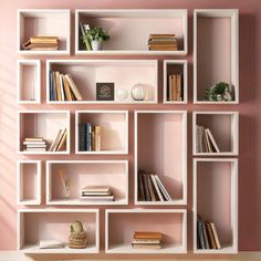 the shelves are filled with books and vases on top of each other in front of a pink wall