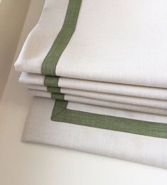 four folded white sheets with green trim on them