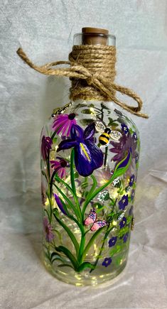 a glass bottle with flowers painted on the outside and string tied to it's top