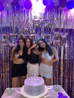 three women standing in front of a birthday cake