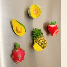 various fruits and vegetables are arranged on a stainless steel counter top, including an avocado, pineapple, strawberry, kiwi, melon