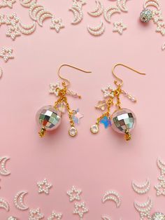 These 14K gold-plated disco ball dangle earrings with star and faux crystal charms are the perfect accessory for a raucous night out. Whether you want to dance with somebody or dance all by yourself, these maximalist beauties will catch light and shine bright. They also make the perfect gift for your dance-aholic bestie or a diva bachelorette.  Drop Length: 2 inches Care Instructions: These earrings are handmade with nickel-free gold-plated stainless steel. Gold-plated jewelry is susceptible to tarnishing if exposed to lotion or oils, so I recommend moisturizing and adding any fragrance before wearing. * Due to different settings on computer monitors and mobile devices, colors that appear on your screen may vary slightly from the actual product. Love this? Check out more Offkilter Co jewel Disco Ball Jewelry, 70s Jewelry Disco, Maximalist Earrings, New Years Jewelry, Disco Jewelry, Disco Ball Earrings, Silver Disco Ball, Star Festival, 70s Jewelry