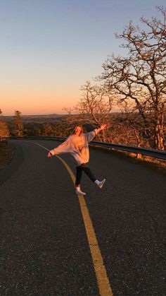 a person jumping in the air on a road with trees and hills in the background