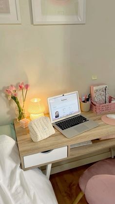 a laptop computer sitting on top of a wooden desk next to a pink chair and lamp