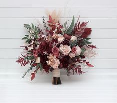 a bouquet of flowers and greenery in front of a white wall