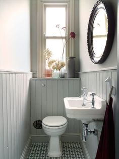 a white toilet sitting next to a sink in a bathroom under a mirror above a window