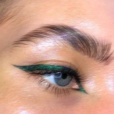 a woman's eye with green and black makeup on top of her lashes, looking down at the camera