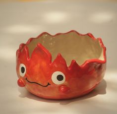 a red ceramic bowl with eyes and mouth on the table next to a white surface