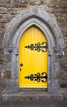 a yellow door is in an old stone building with arched window and iron work on it