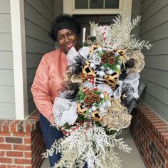 a woman standing in front of a house holding a christmas wreath