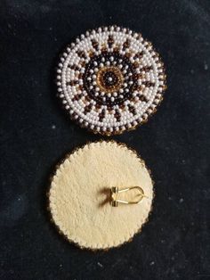 two beaded objects sitting next to each other on a black surface with a gold hook