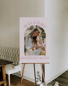 a welcome sign is on an easel in front of a white couch and table