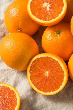 several oranges cut in half sitting on top of a white cloth with one whole and two halves missing