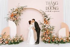 a bride and groom standing in front of a floral arch with the words thang duong on it