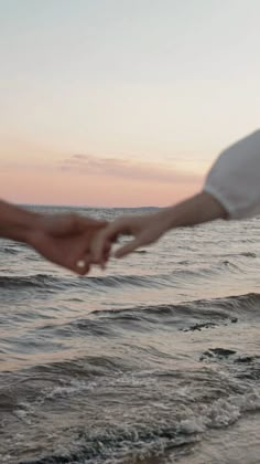 two people holding hands on the beach at sunset