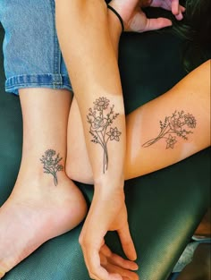 two women with matching tattoos on their legs, one holding flowers and the other sitting down