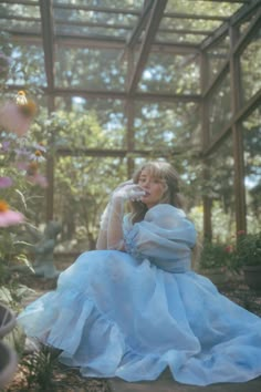 a woman in a blue dress sitting on the ground next to some flowers and plants