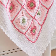 a pink and white crocheted blanket with flowers on it