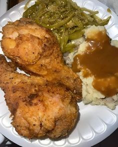 a white plate topped with fried chicken, mashed potatoes and green beans covered in gravy