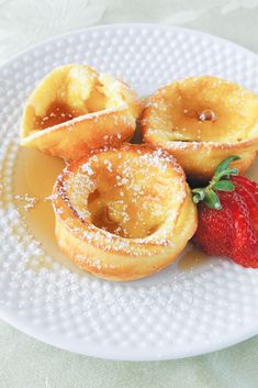 a white plate topped with donuts covered in powdered sugar next to a strawberry