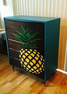 a pineapple painted on the side of a wooden cabinet in a room with hard wood flooring